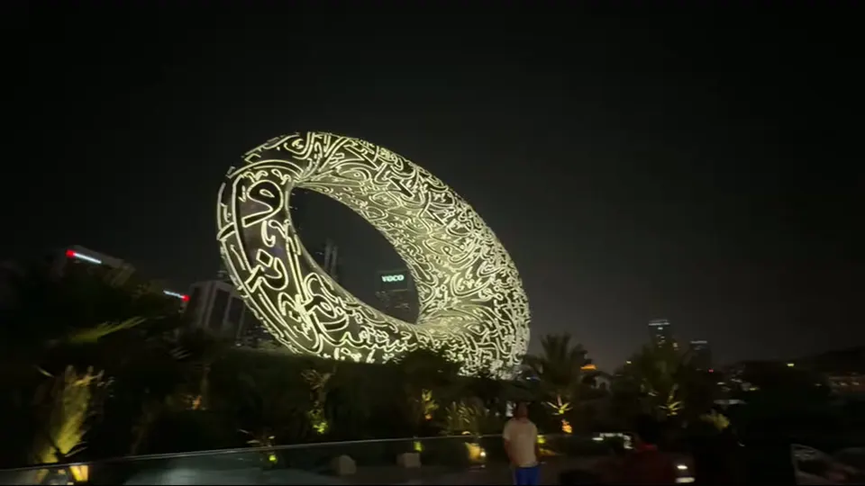 Wide night view of the illuminated Museum of the Future above landscaped grounds.