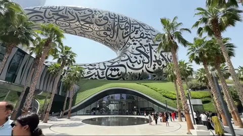 Ground-level view of the Museum of the Future with palms and curved grassy entrance.